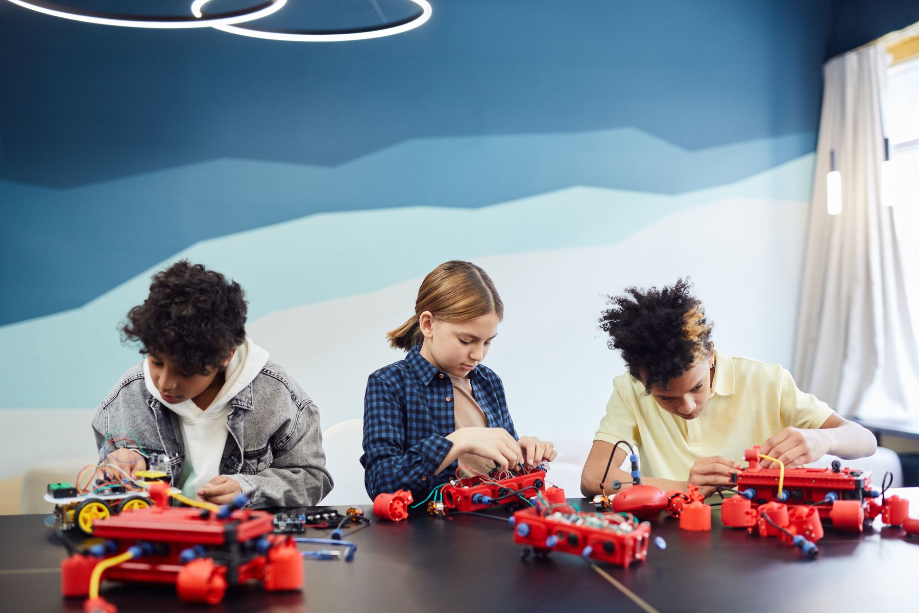 Tres alumnos arman robots sobre una mesa larga en el salón de robótica